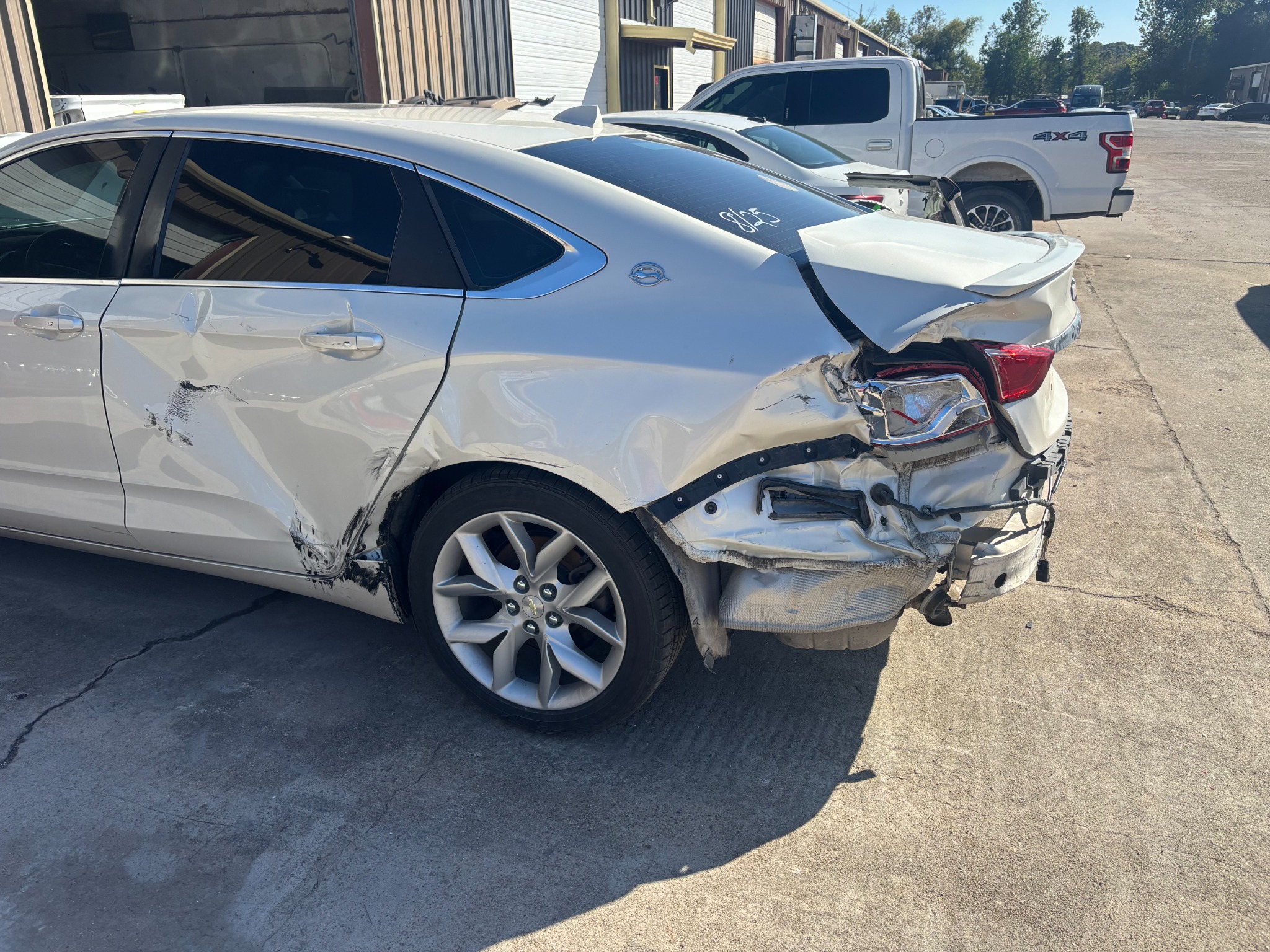 White Chevrolet Impala before repair, with damage to the left rear quarter, rear door and trunk.